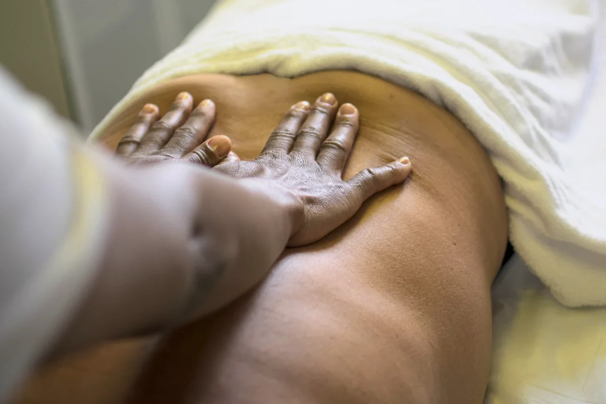 Hands massaging a client's lower back, with a towel over the hips.