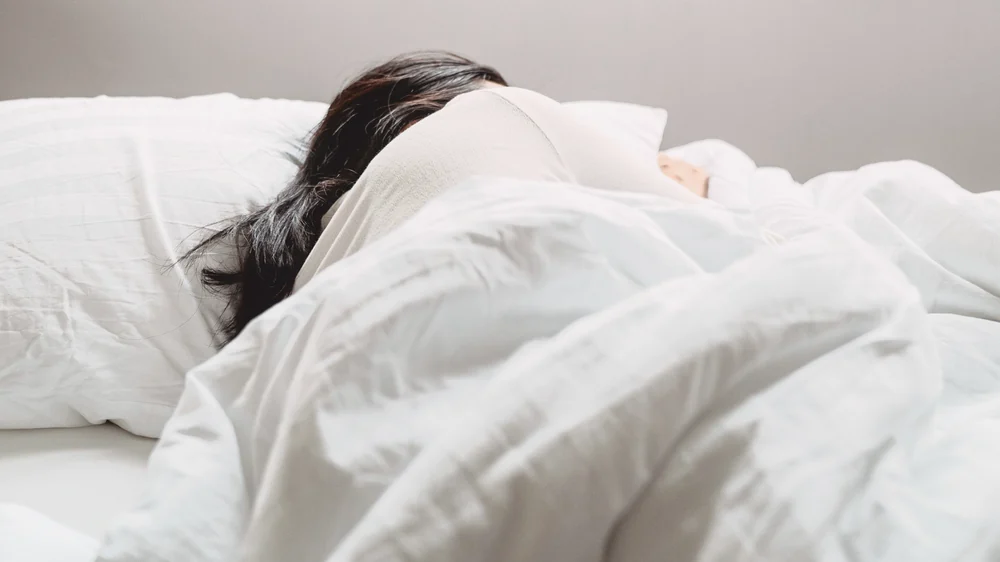A woman with dark hair resting in white bedding