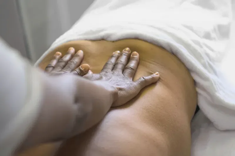 Hands massaging a person’s lower back, a towel over the hips
