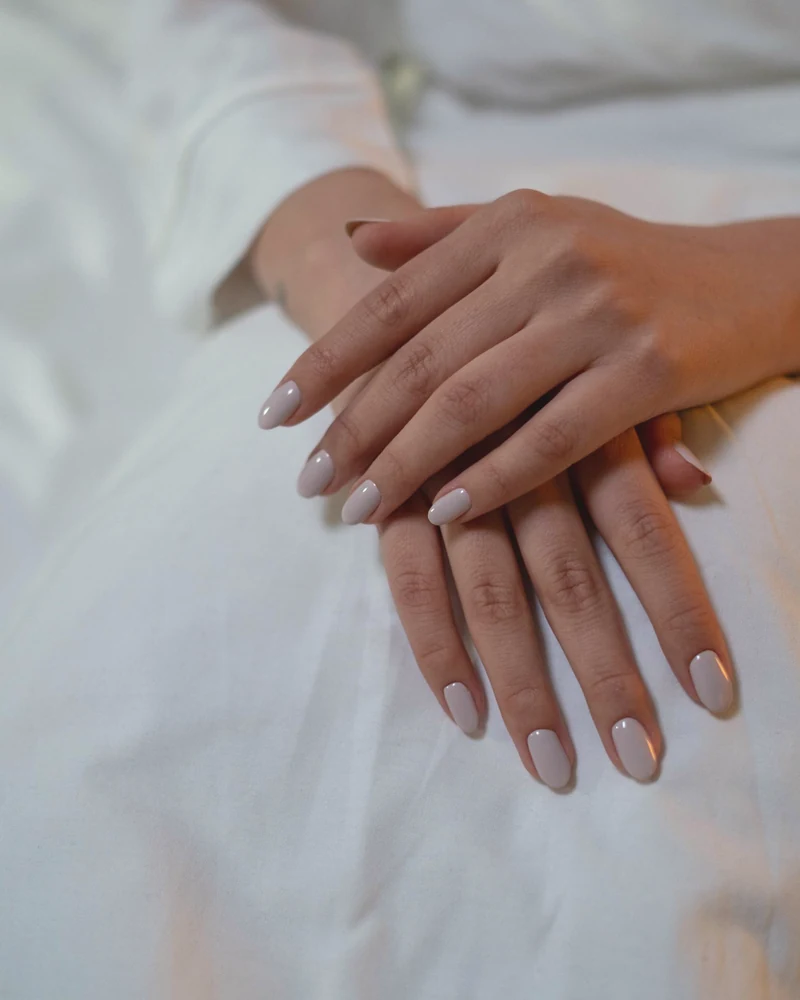 Hands resting on white linen, the nails neat and nude
