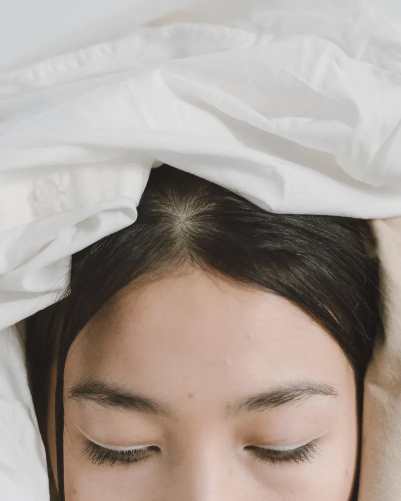 A woman at rest with her eyes closed, a white towel wrapped around her hair
