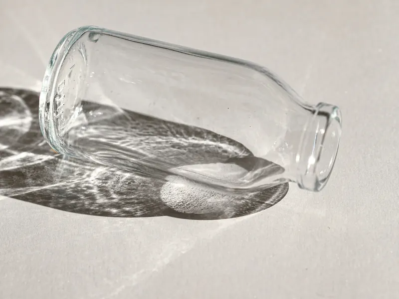 A clear glass bottle lying on its side in sunlight, its shadow rippled with light